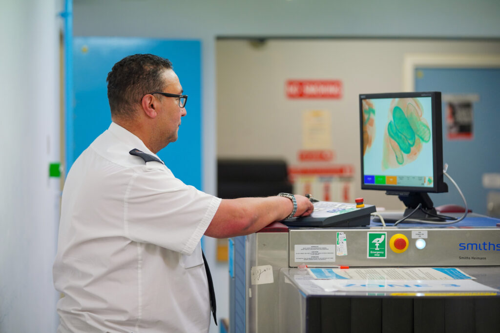 A man stands in front of a display screen showing the results of a scanned bag