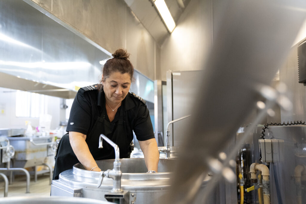Female caterer in a prison kitchen using industrial sized kitchen equipment