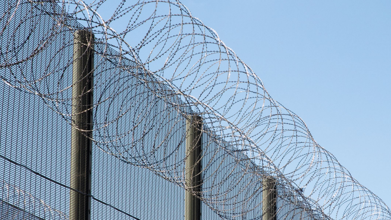 Photograph of some barbed wire at the top of a prison fence.
