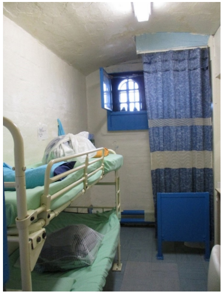An image of a crowded cell in HMP Leeds with bunk beds and a curtain screening the toilet by the window.