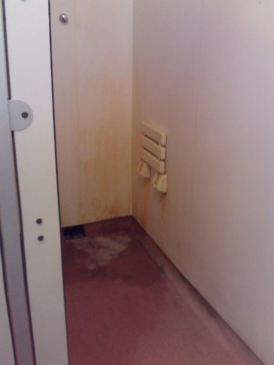 Photograph of the showers on A wing, focusing on a single cubicle which has a worn floor in need of cleaning or renewal.