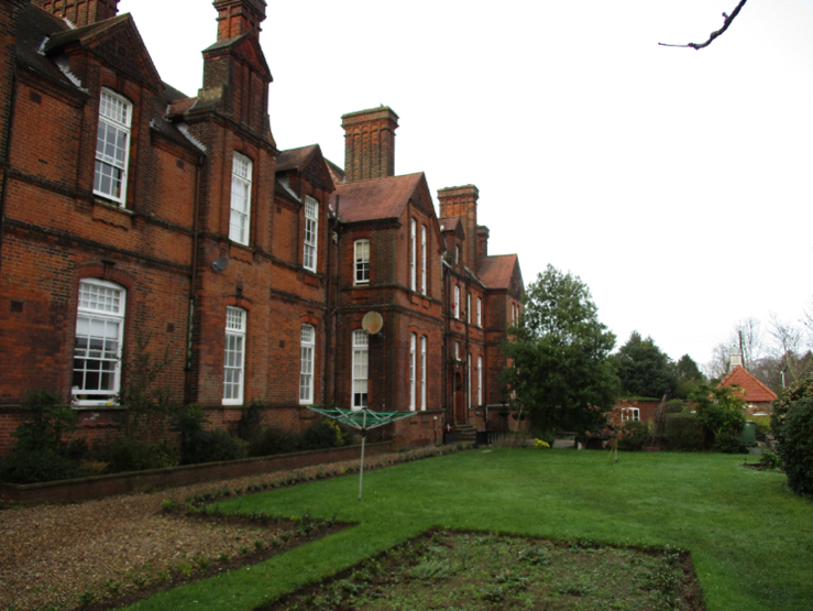 Photograph of the exterior of Britannia House, a two-storey brick building, with a grass area with shrubs to one side.