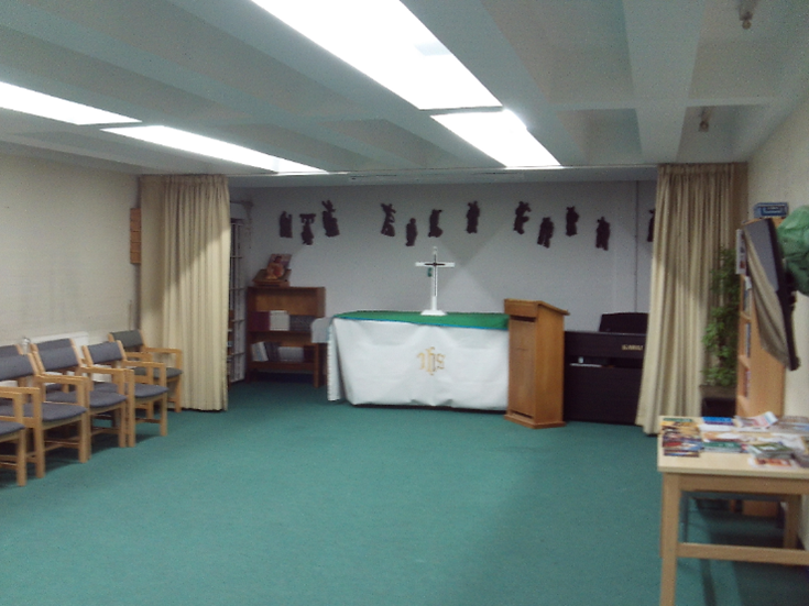 Photograph of the Category C multi-faith room. There is an altar at the back, with a table upon which stands a cross. Chairs, a lectern and a table are among the other items of furniture arranged around the perimeter of the room.