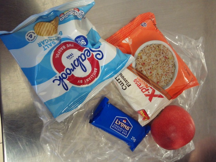Photograph of a 'healthy lunch' featuring crisps, biscuits, a cereal bar, and an apple.