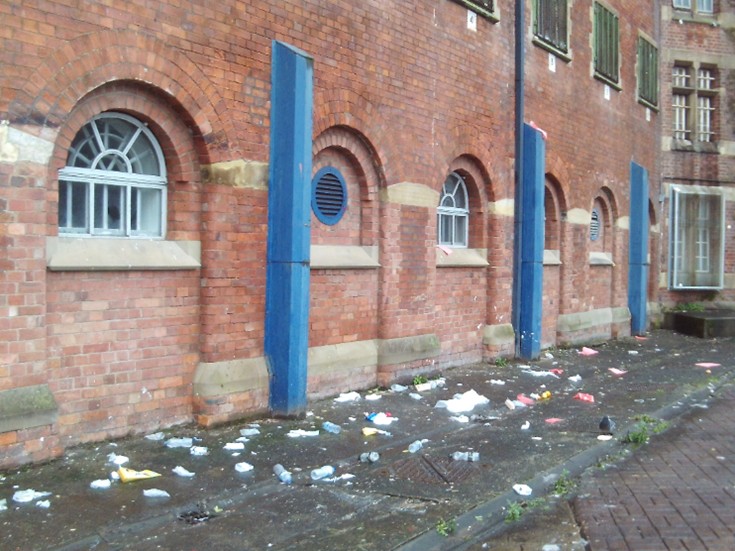 Photograph of an exercise yard, with lots of litter on the ground near the building.
