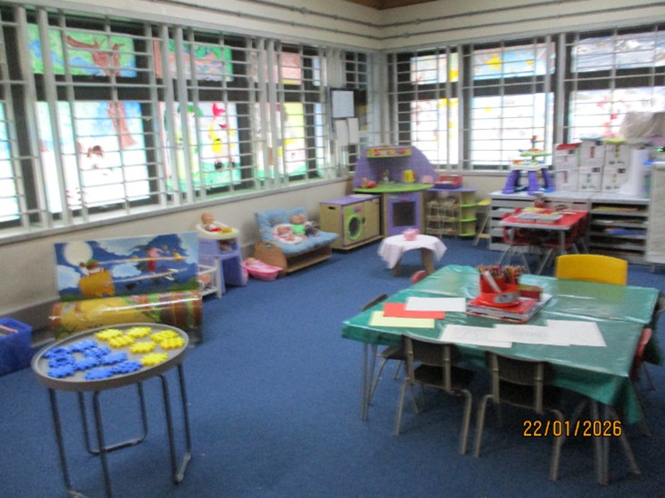 Photograph of the play area in the visits hall, featuring a table with art materials on it in the centre and toys arranged around the perimeter of the room.