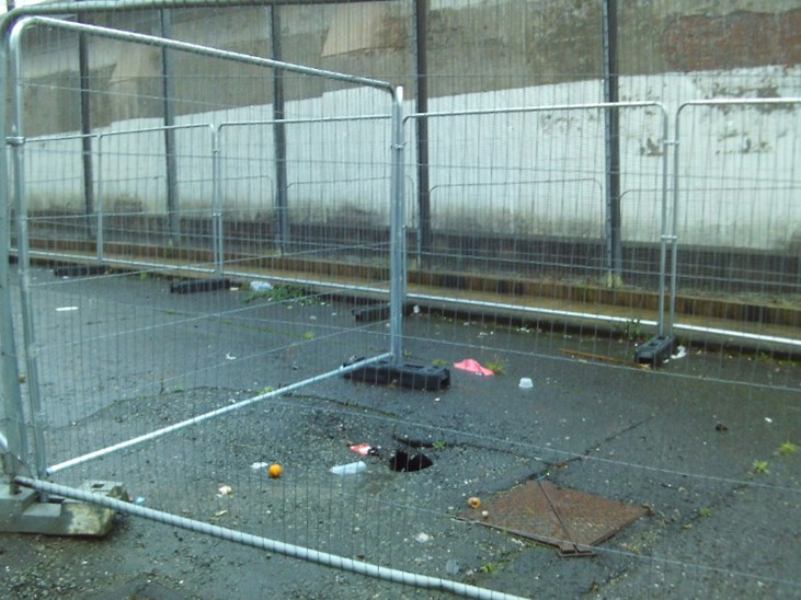 Photograph of a concreted area, with a large pothole in it. A fence has been erected around the pothole.