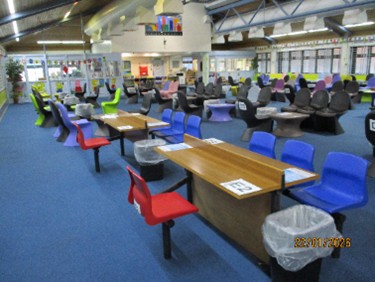 Photograph of the visits hall, with tables and chairs arranged in rows down the length of the room. The carpet is blue.