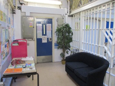 Photograph of a waiting room. There is a sofa to one side and a desk with leaflets on it to the other side.