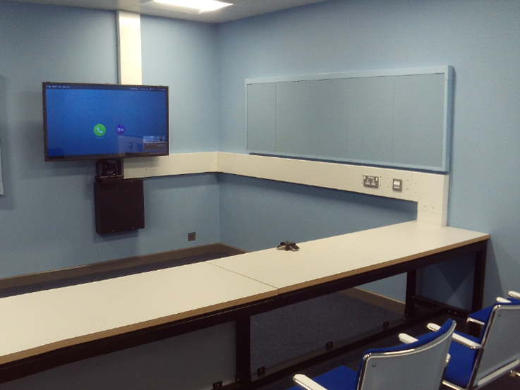 Photograph of the OVC suite, with a wall-mounted screen and a long table behind which chairs are arranged in a row.