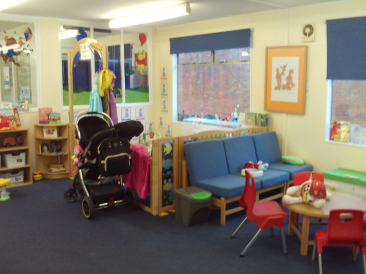 Photograph of the visitor centre play area. The walls are decorated with pictures and lots of play equipment is visible. there are some blue easy chairs and a low table with chairs arranged around it.