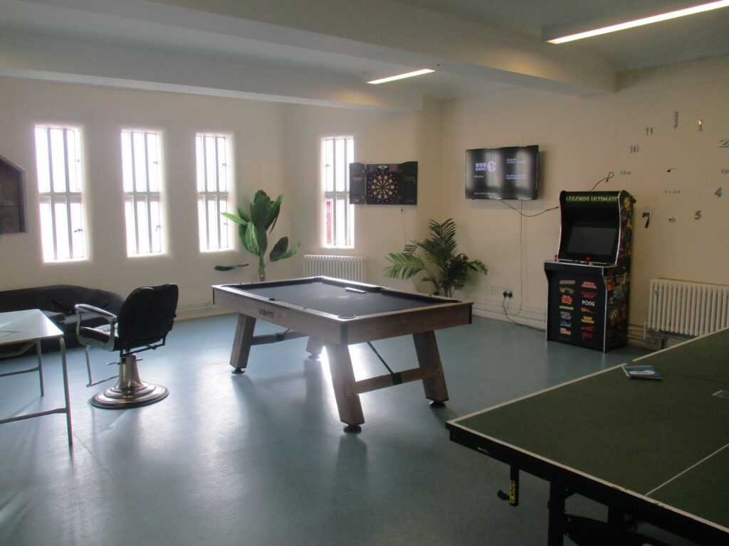 Photograph of the association area on the ISFL unit. There is a pool table, a table tennis table and an video arcade game machine, and some chairs are visible.