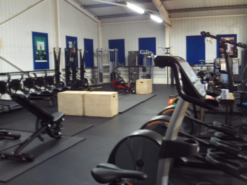 Photograph of an area of the gym in which a variety of exercise equipment is lined up in rows.