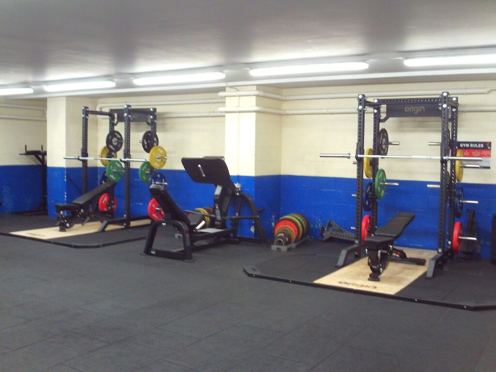 Photograph of the weights area in the gym. Benches and machines are arranged down one wall.