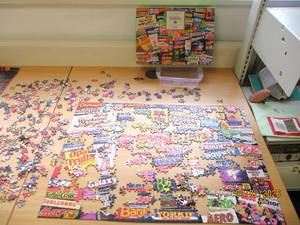 Photograph of the games area in the library, with an in-progress giant jigsaw laid out on the floor.