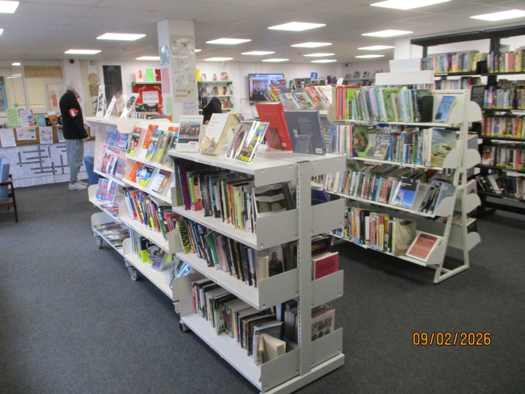 Photograph of the area of the library dominated by shelves of books. The shelves are of a variety of designs and all are well-stocked with publications.