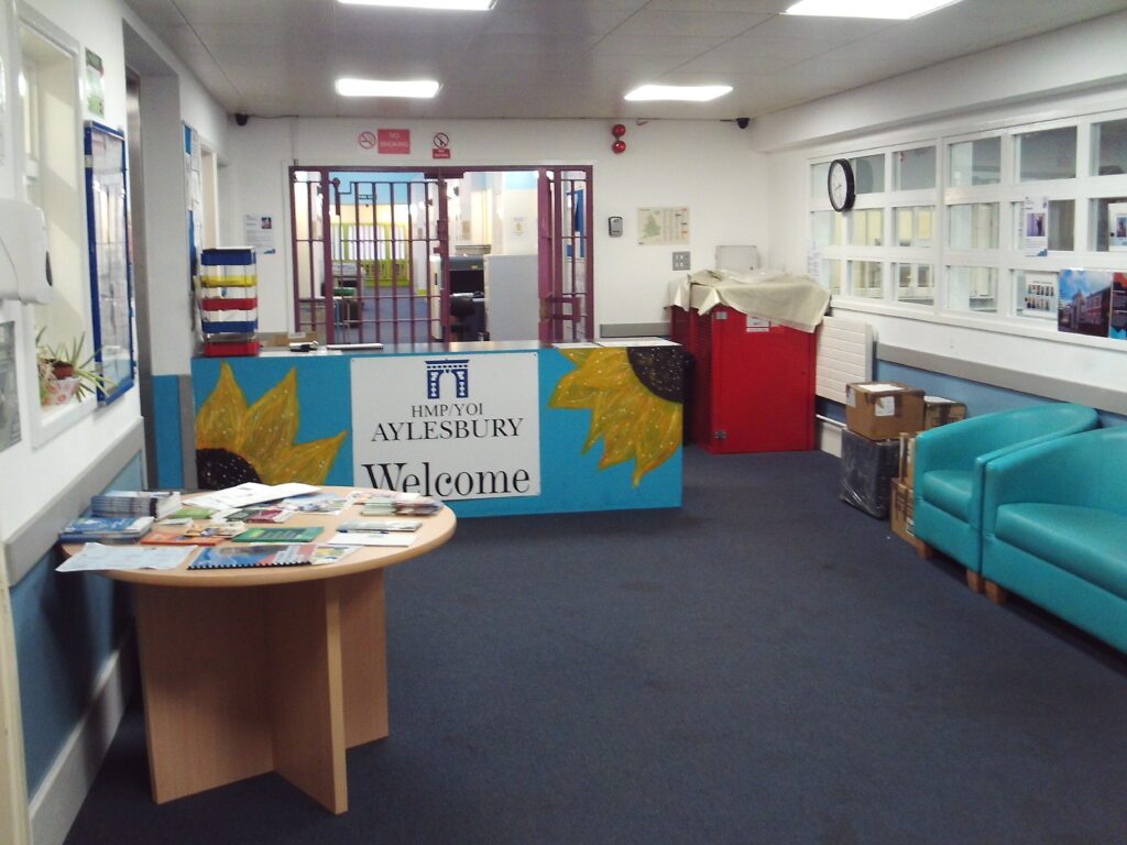 Photograph of the interior of the reception area. The area is brightened with decoration and displays on the walls and the counter, there is a table to one side with literature on it, and to the other side there are some chairs upholstered in an aquamarine-coloured fabric.