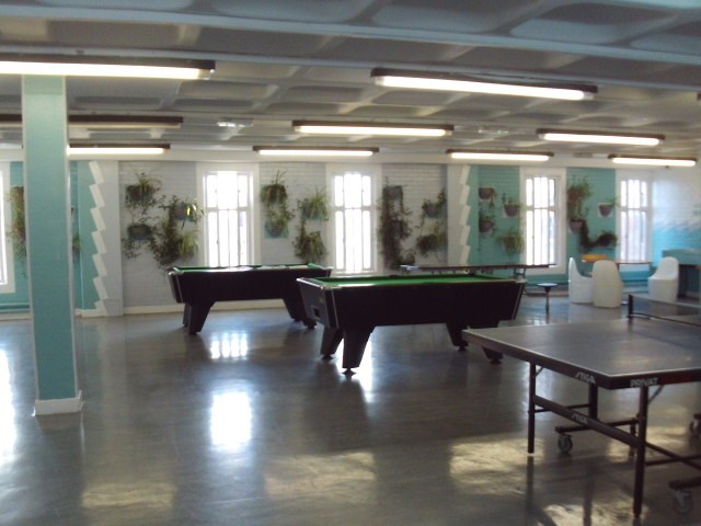 Photograph of the C wing association area, which features two pool tables and a table tennis table. Some of the walls have been painted with murals and there are floor-to-ceiling windows.