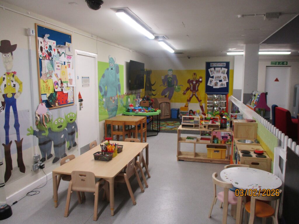 Photograph of the children's play area in visits  There are some low tables with chairs around them, some paly equipment and several large wall murals.