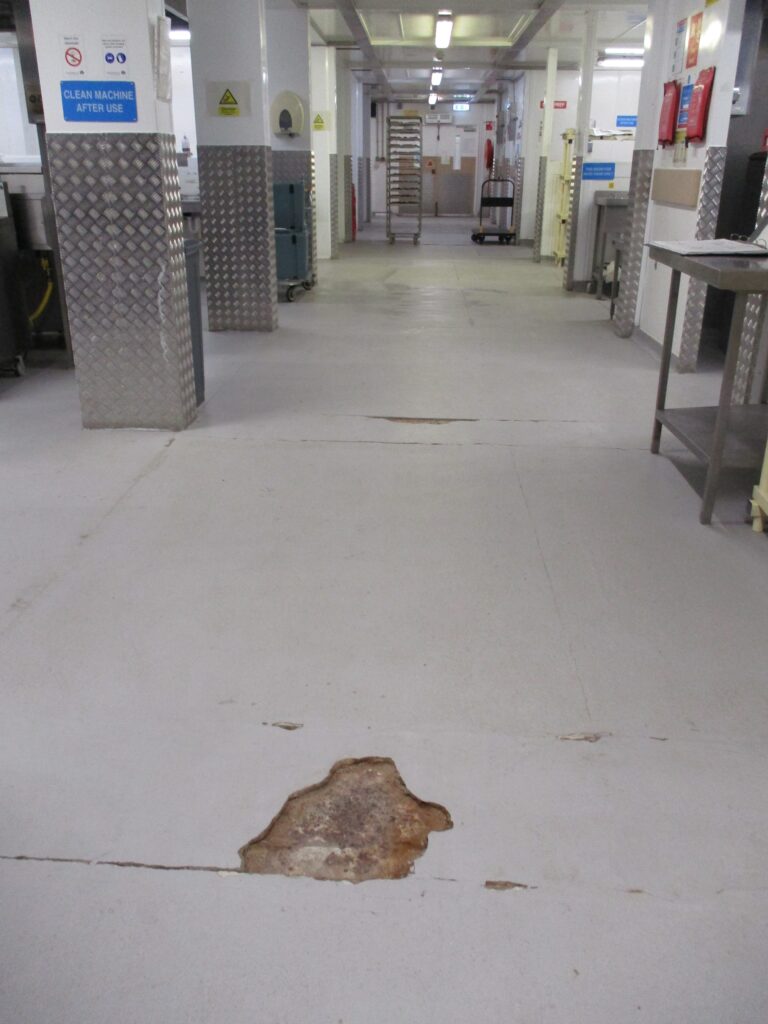 Photograph of damaged flooring in the main kitchen. A large sction of the floor covering has been chipped away.