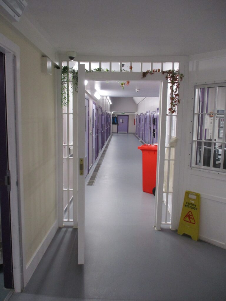 Photograph of the segregation unit interior, looking through a doorway down a corridor on either side of which cell doors can be seen in the walls.