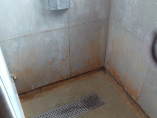 Photograph of a shower in the first night centre. Water damage is visible on the walls and floor of the cubicle.