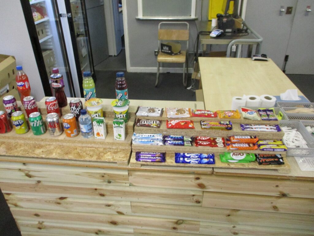 Close-up photograph of the visits hall canteen counter, focusing on a specific section stocked with products including confectionery, tissues and drinks.