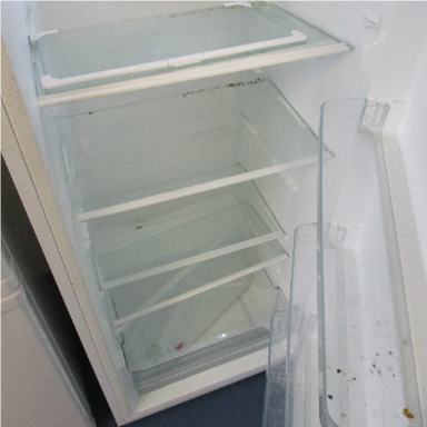 Photograph of an empty refrigerator interior showing multiple clear glass shelves and a transparent door compartment with some dirt and stains. 