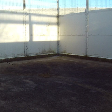 Photograph of the CSRU exercise yard, showing an empty outdoor corner enclosed by white metal fencing with visible rust and dirt marks near the base.