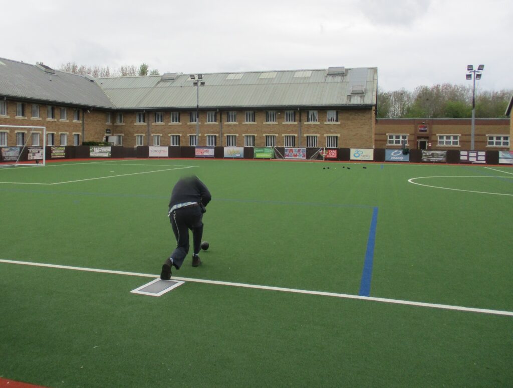 Photograph of prisoners playing bowls on an astroturf sports pitch.