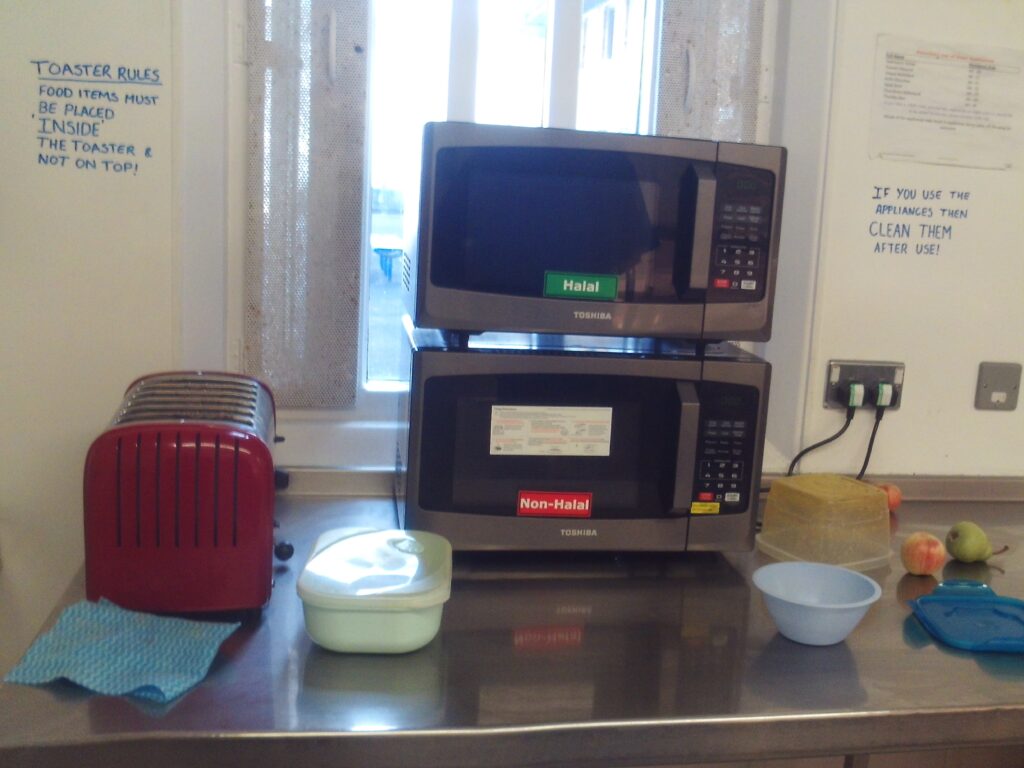 Photograph of some of the self-catering facilities on a residential unit. There are two microwaves, a taoster and some food containers.