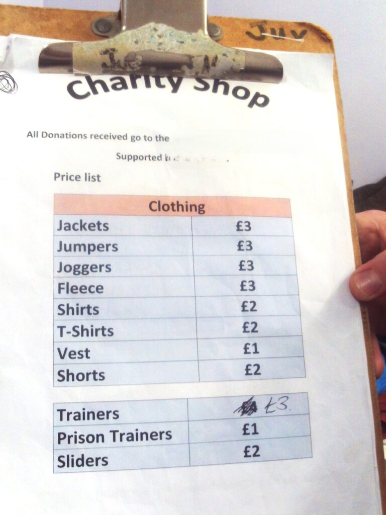 Photograph of the charity shop price list, a piece of paper on a clipboard with prices for the different types of clothing available.
