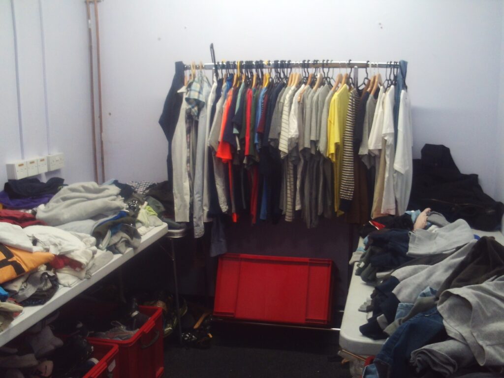 Photograph of the charity shop, with a hanging rail full of cloths, and more items displayed on tables