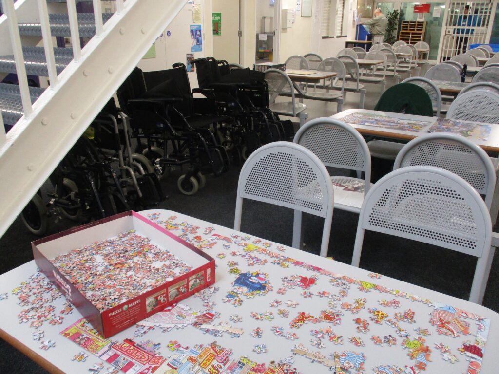 Photograph of a table on which there is a partially completed jigsaw. Many pieces are on the table itself, with many more still in the box awaiting placement.