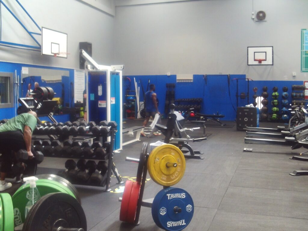 Photograph of the weights room at the gym, with a wide range of equipment on display. Basketball hoops are mounted on the walls.