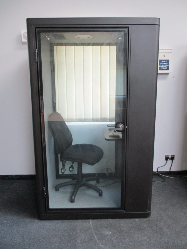 Photograph of the photo booth in the visits hall, a telephone box style kiosk with a chair in it.