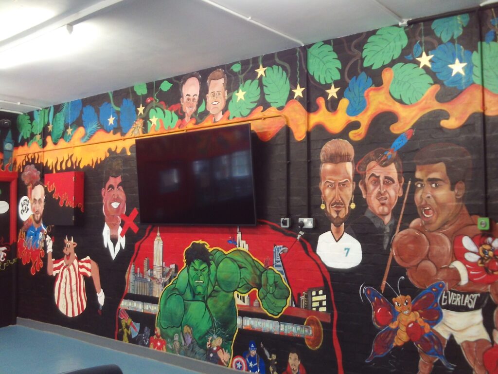 Photograph of colourful murals covering a wall on the resettlement unit, It features many themes and objects.