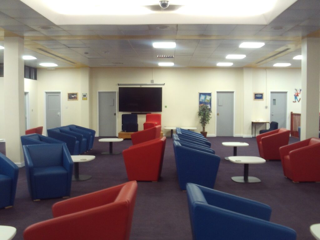 Photograph of the visits area in the Pankhurt unit. Blue and red chairs are arranged around coffee tables in rows.