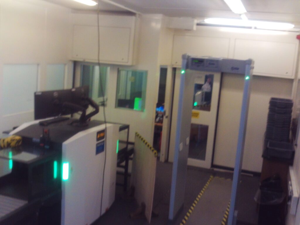 Photograph of the gate searching room, with scanning machines for objects and people.
