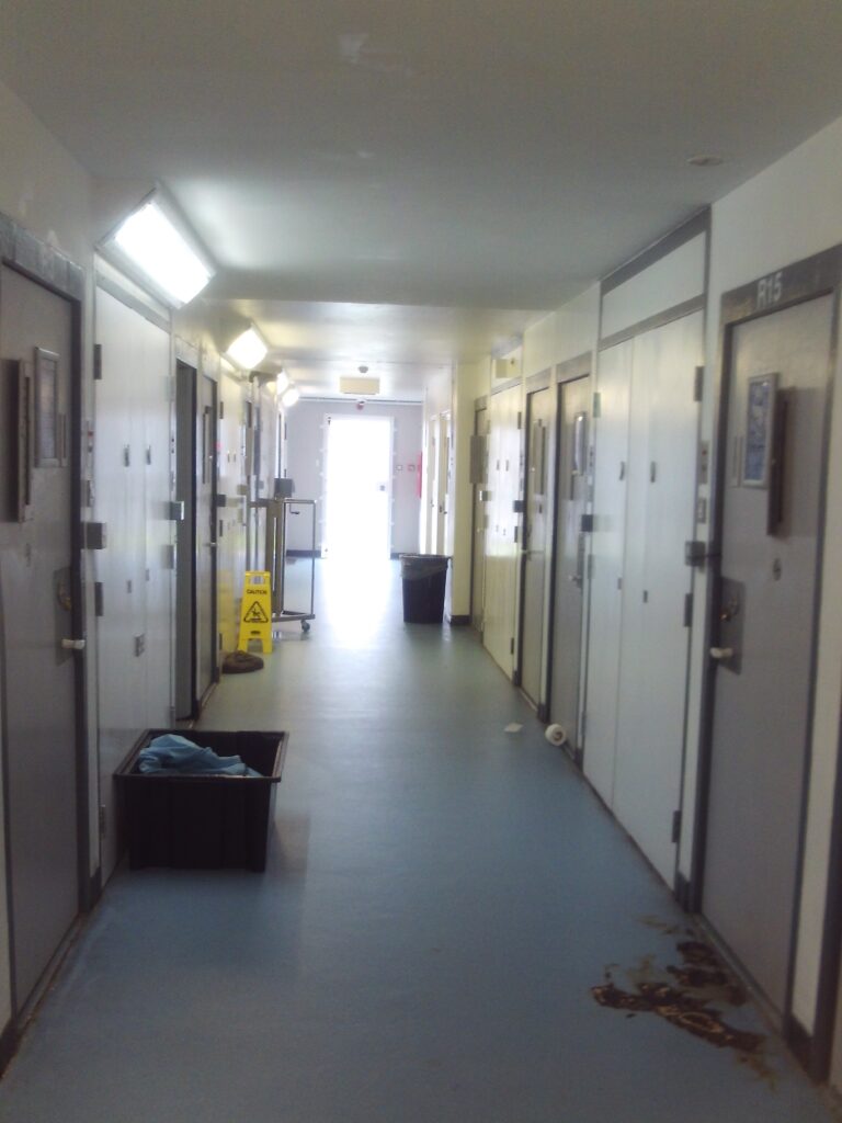 Photograph of the segregation unit corridor. Doors can be seen on both sides and there is a bright light at the far end.