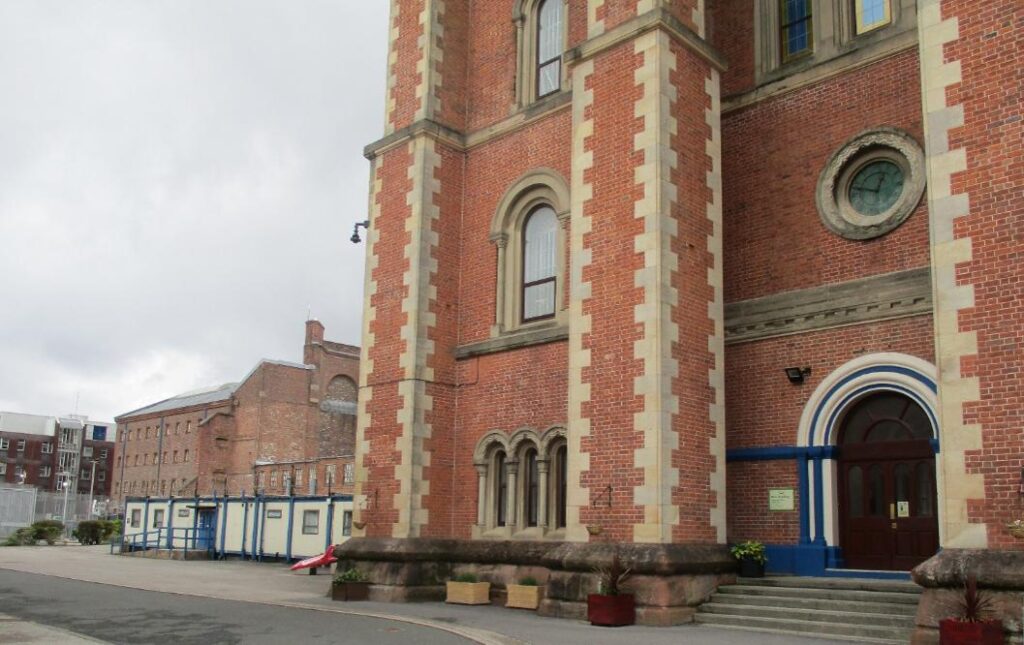 Photograph of the main gatehouse at Liverpool prison, with other blocks to the side, behind a perimeter fence. The buildings look largely Victorian.