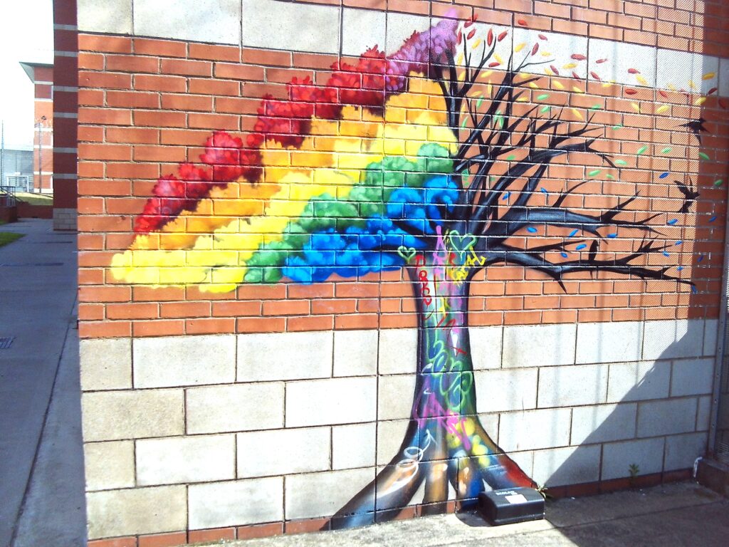 Photograph of a mural on a wall outside L and M wings. It depicts a tree that has rainbow-coloured leaves on it.