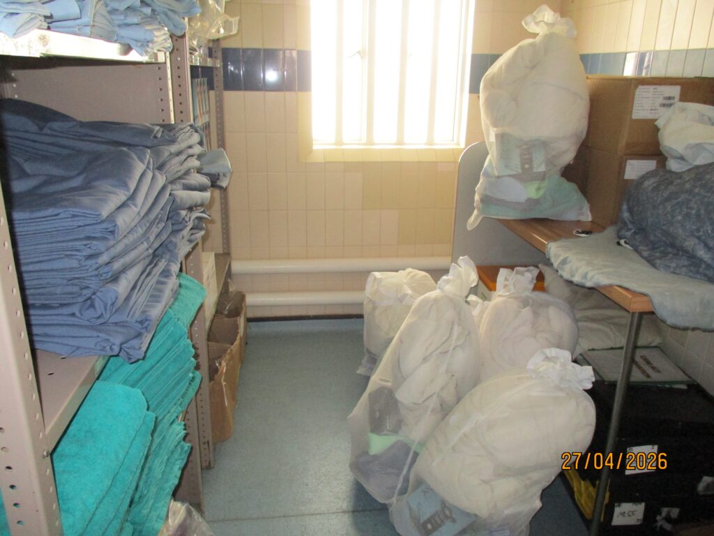 Photo of first night packs stacked in a small storeroom ready to be issued. Towels are stacked in shelves on one side of the room.