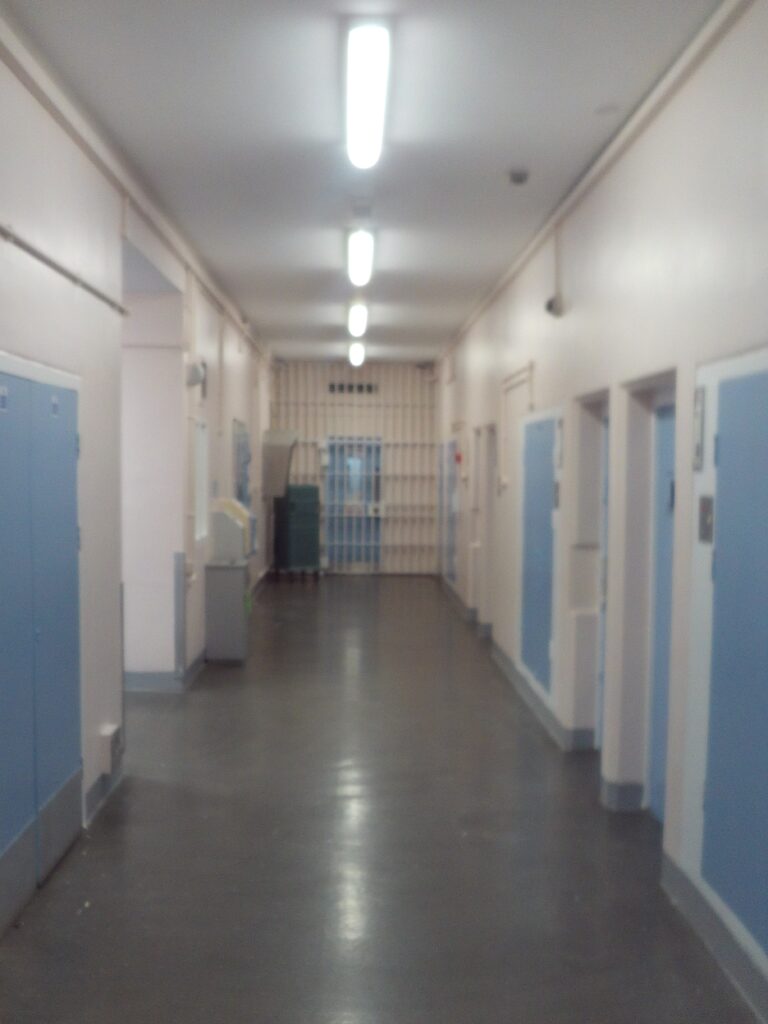 Photograph of the corridor in the in-patient unit. the walls are painted white and blue doors can be seen on either side.