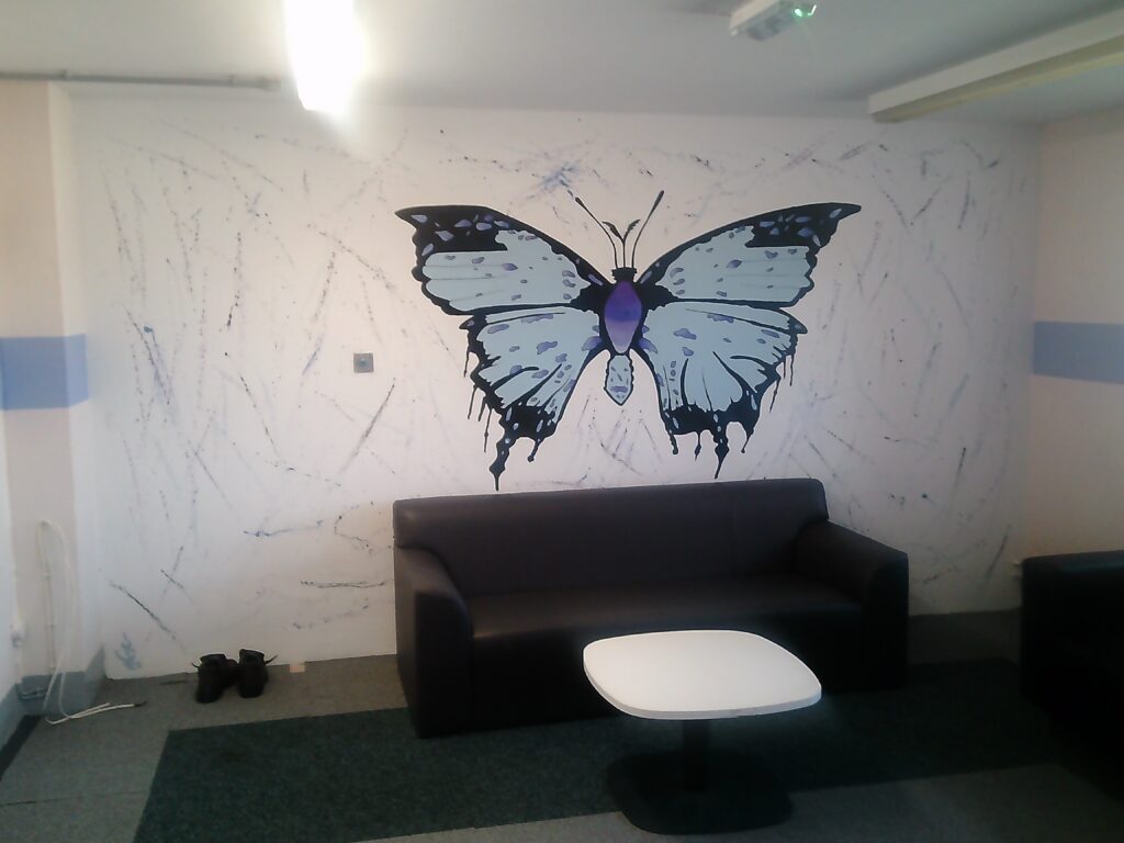 Photograph of the induction unit. A sofa is positioned behind a coffee table and there is a large painting of a butterfly on the wall behind it.