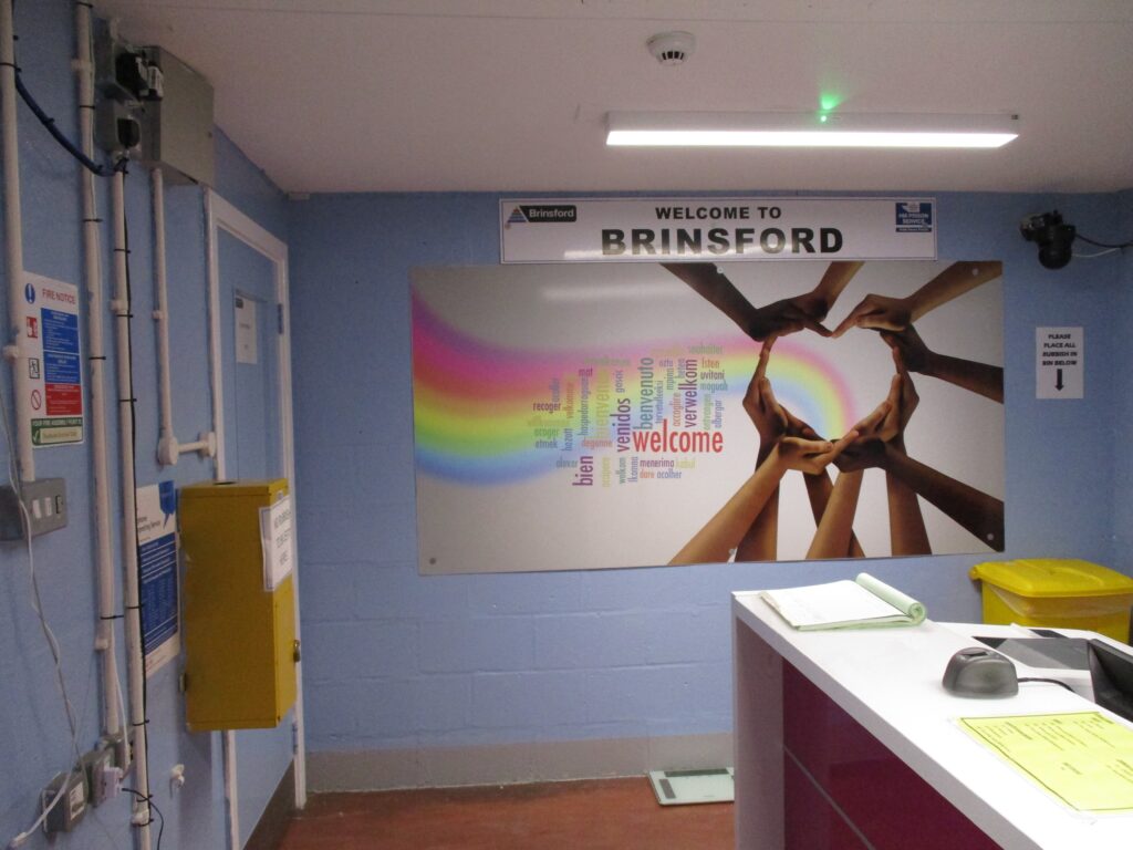Photograph of the reception area. There is a desk to one side and on the walls there are signs and information displays, including one colourful mural.