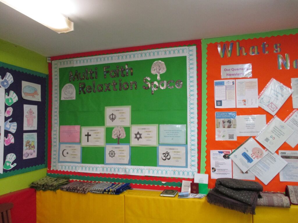 Photograph of the multi-faith relaxation area. There are information displays on the wall and prayer mats on a shelf.