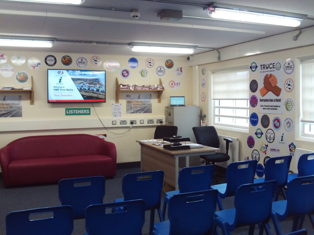 Photograph of the induction room. There is a screen mounted on the wall at the front with a desk for the presenter, and rows of chairs are arranged facing the screen.