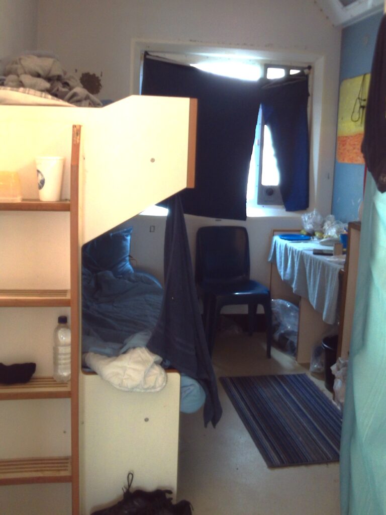 Photograph of a doubled-up cell with bunk beds, a desk and book shelf visible.