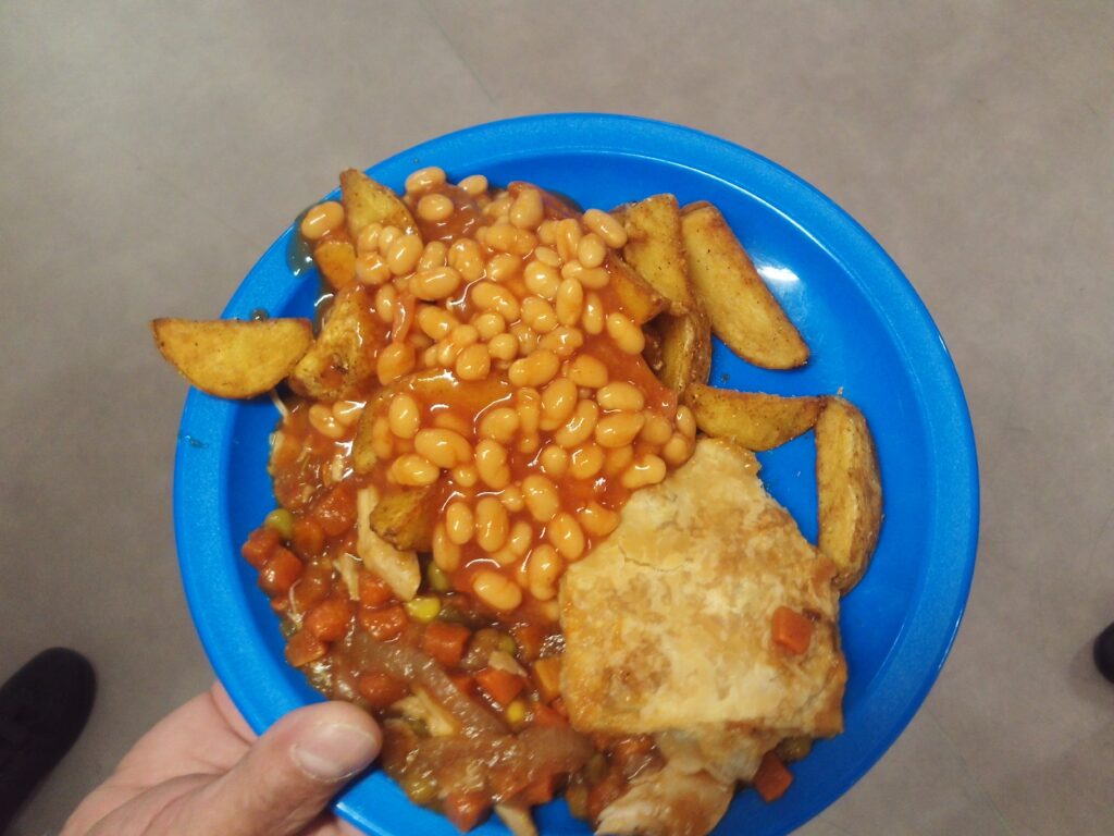 Photograph of an evening meal, featuring baked beans, chips, and some chopped vegetables on a blue plate.